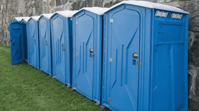 Row of blue portable toilets lined up on grass against a stone wall for event sanitation in Marietta, GA