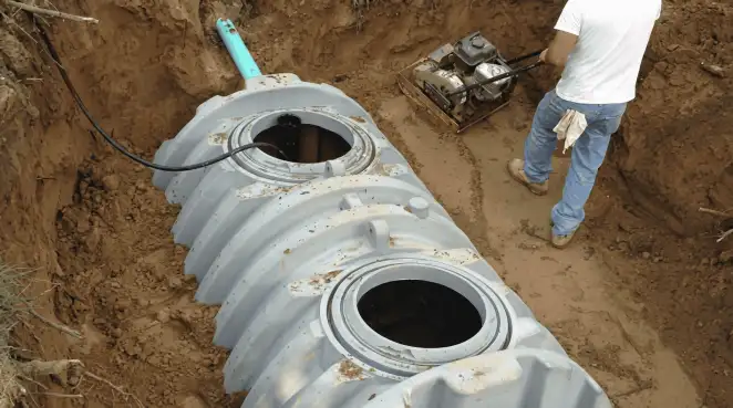 Septic tank installation showing a technician compacting soil around a new poly septic tank in an excavation pit in Marietta, GA